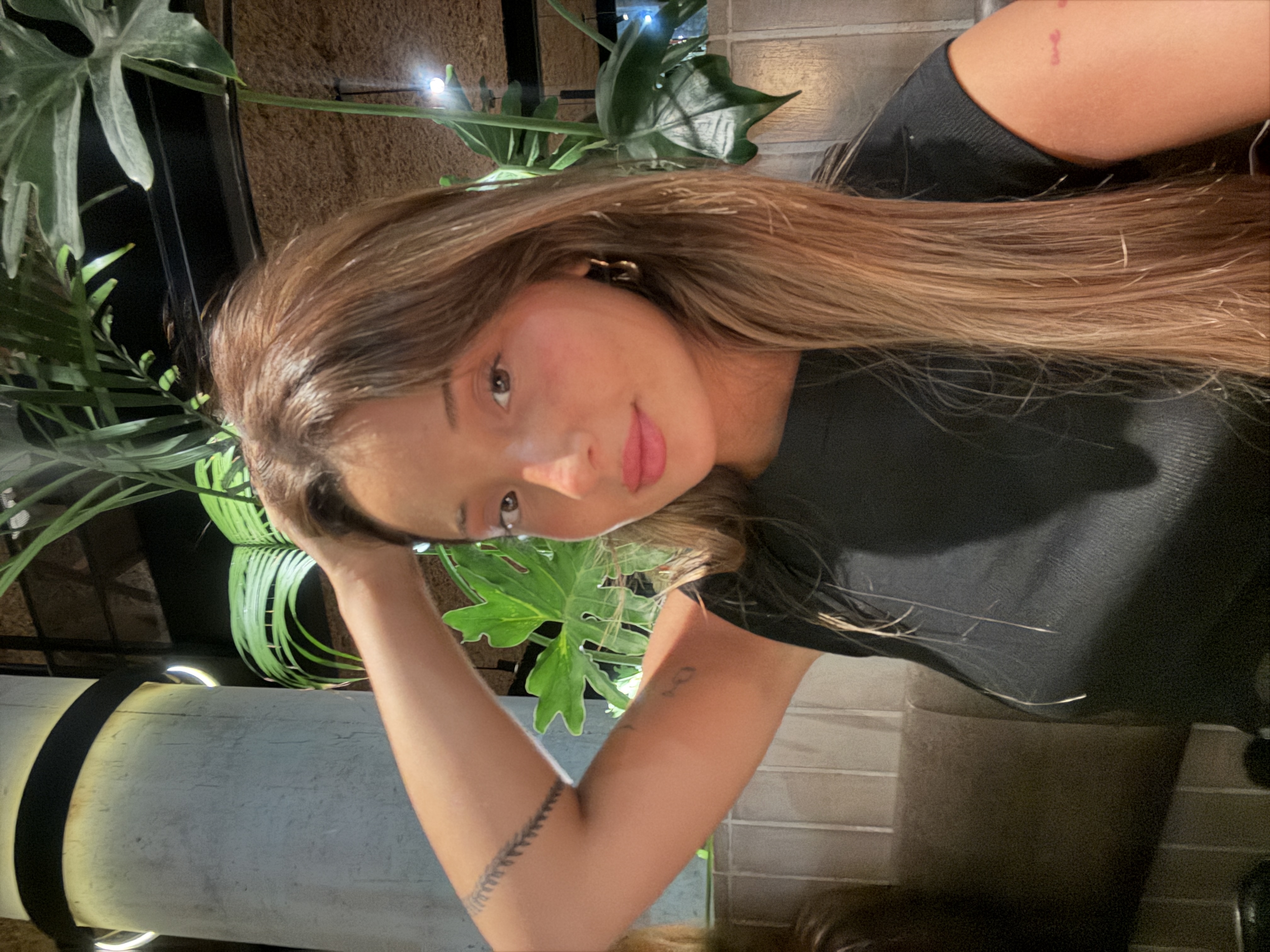 Camila in a black top with gold hoops at a dimly lit restaurant surrounded by plants